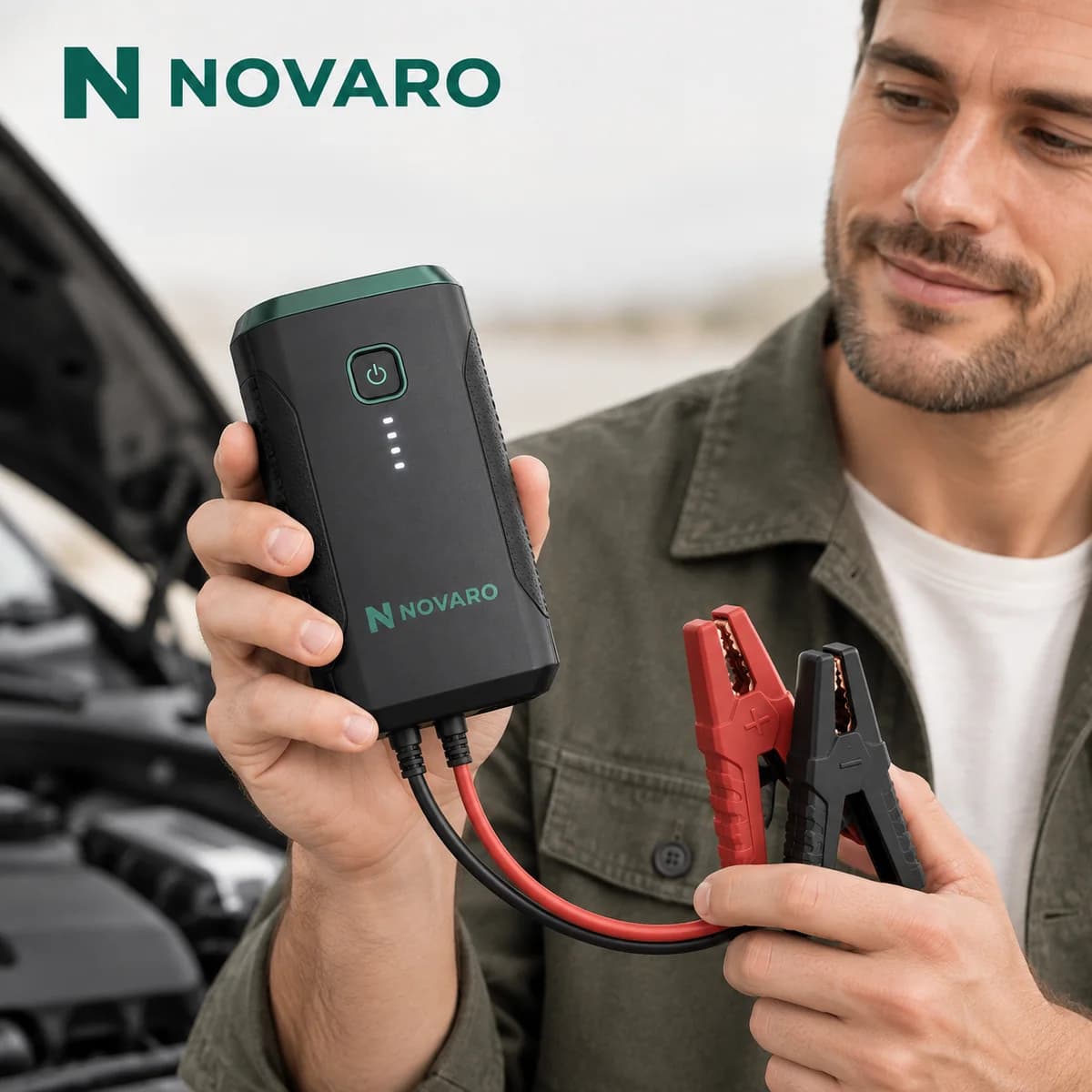Man holding the NOVARO Portable Car Jump Starter with clamps attached in front of an open car hood
